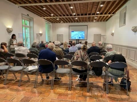 Salle de réunion avec 7 écrans, participants attentifs et une intervenante, ambiance professionnelle.