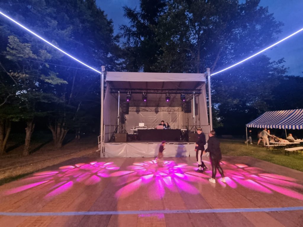 Scène festive à Bougival avec éclairage coloré et DJ, entourée de participants dans une ambiance conviviale.