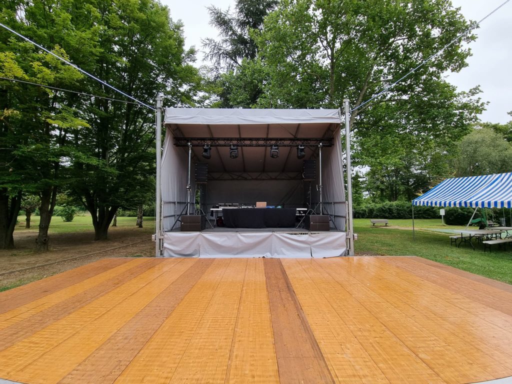 Scène de la fête de Bougival avec équipement audio et éclairage, prête pour le DJ, entourée d'arbres et de tentes.
