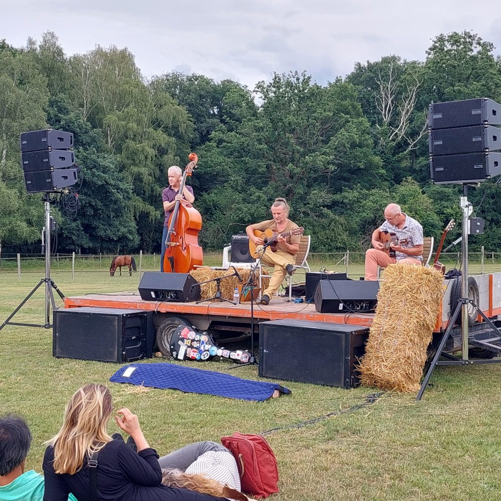 Concert de jazz en plein air avec trois musiciens sur scène, entourés de spectateurs profitant de l'ambiance détendue.