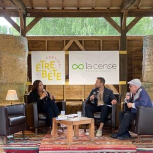 Conférence au Haras de la Cense avec des intervenants assis sur des fauteuils, devant des banderoles de l'événement et de l'organisation.