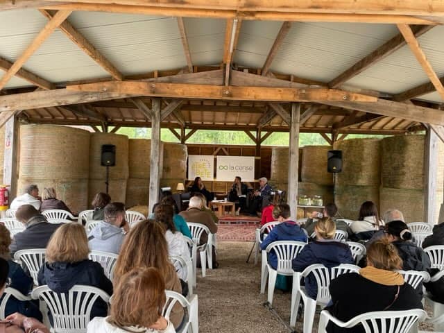 Conférence au Haras de la Cense, avec un public attentif, sous une structure en bois, entourée de bottes de foin.