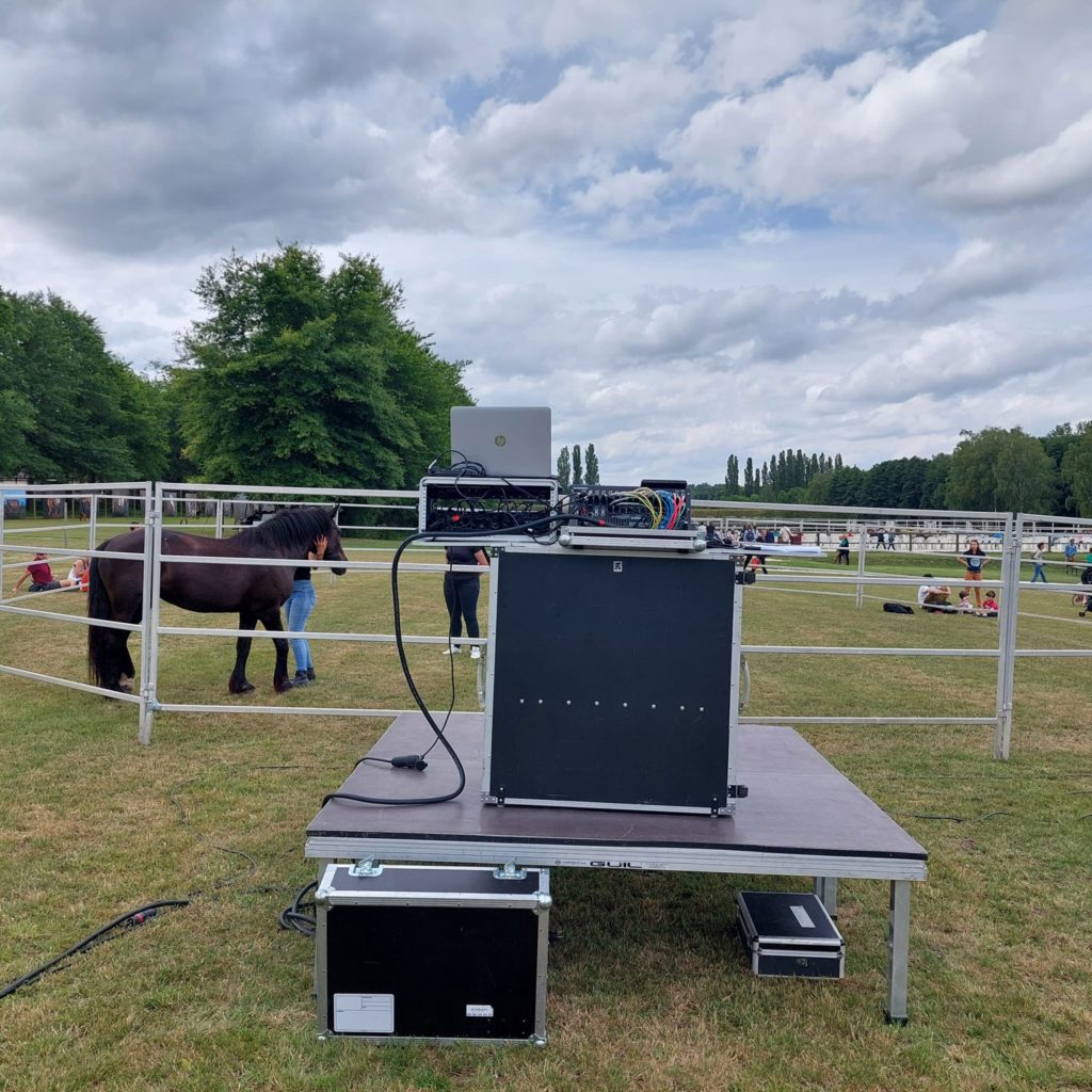 Matériel de sonorisation prêt pour un concert champêtre, avec un cheval en arrière-plan, au Haras de la Cense. 26 juin 2022.