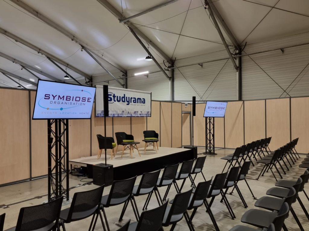 Stand de Studyrama avec écrans Sony Bravia de 55 pouces, logo Symbiose Organisation et chaises disposées pour un événement.
