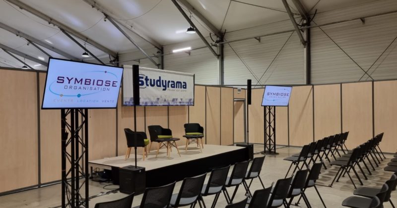 Stand de Studyrama avec écrans Sony Bravia de 55 pouces, logo Symbiose Organisation et chaises disposées pour un événement.