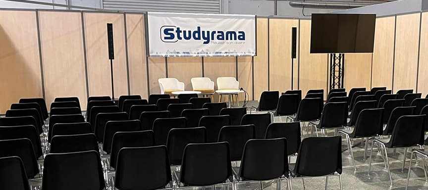 Salle de conférence vide lors du salon Studyrama à Paris, avec chaises noires et écran de présentation.