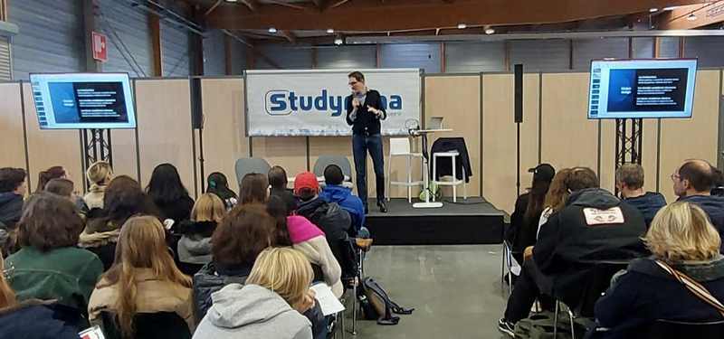 Conférence animée lors du salon d'expo à Paris, avec un intervenant devant un public attentif et des écrans de présentation.