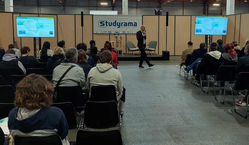 Conférence au salon Studyrama à Paris, avec un orateur présentant devant un public attentif.