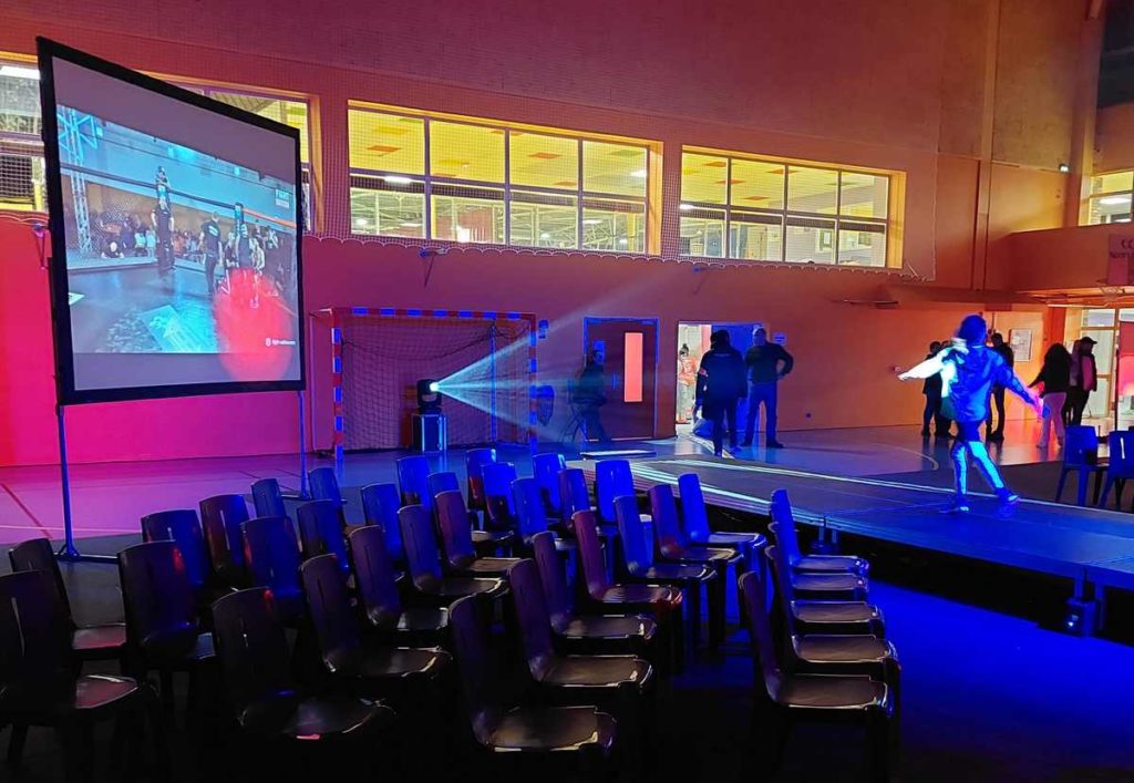 Mise en lumière et sonorisation d'une compétition de MMA, avec un écran projetant un match, dans une salle à Coignières.