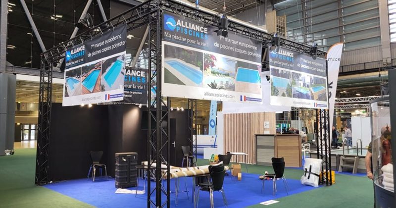 Stand d'Alliance Piscines au salon de Porte de Versailles, mettant en avant leurs produits avec une structure et un éclairage soigné.