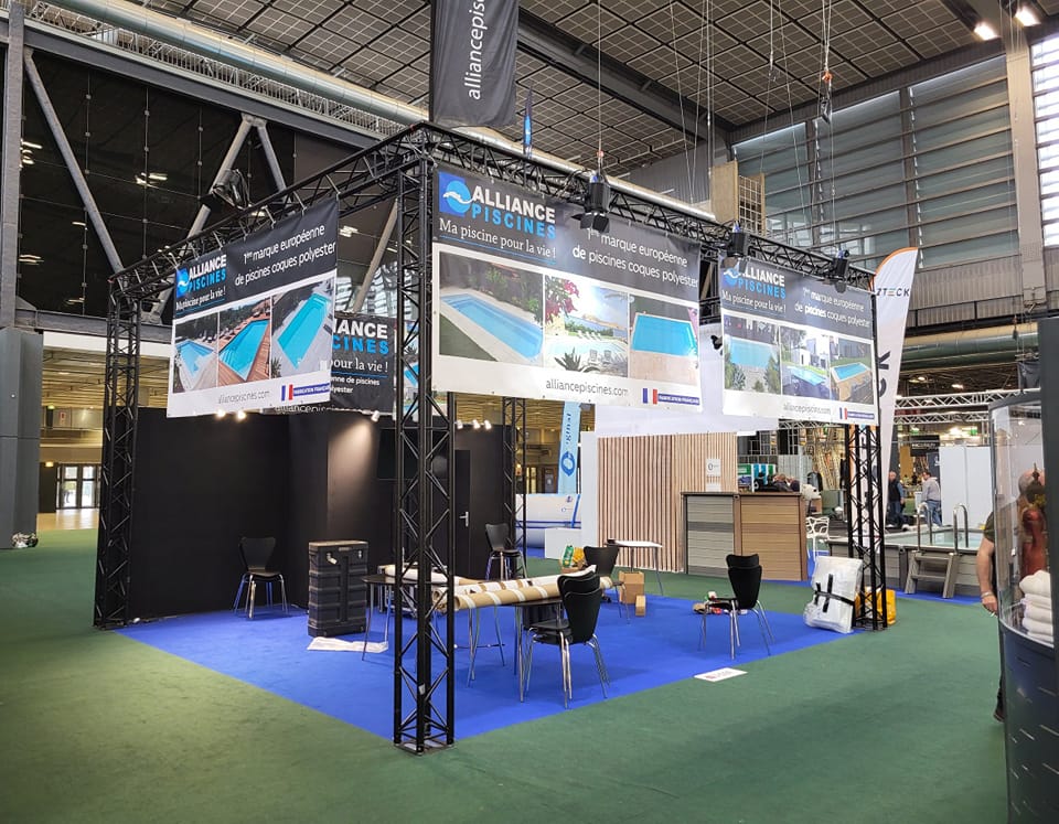 Stand d'Alliance Piscines au salon de Porte de Versailles, mettant en avant leurs produits avec une structure et un éclairage soigné.