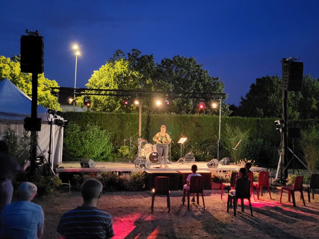 Concert en plein air à Coignières, le 21 juin 2023, avec une artiste sur scène et un public assis devant.