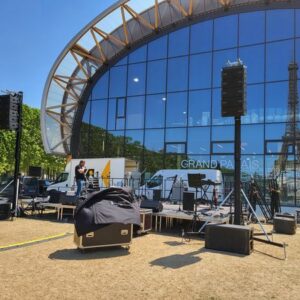 Installation de matériel sonore et d'éclairage presque terminée sur le Champ de Mars, avec la tour Eiffel en arrière-plan.