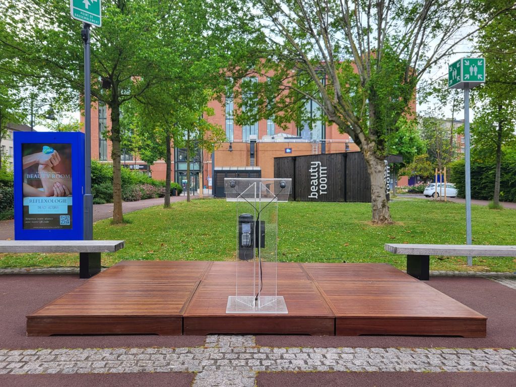 Installation d'une scène avec estrade et panneau "Beauty Room" dans un parc, prête pour un événement.