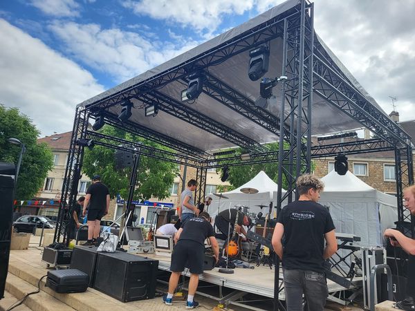 Scène couverte avec son et lumières en cours de montage pour un événement, avec équipements de sonorisation et éclairage.