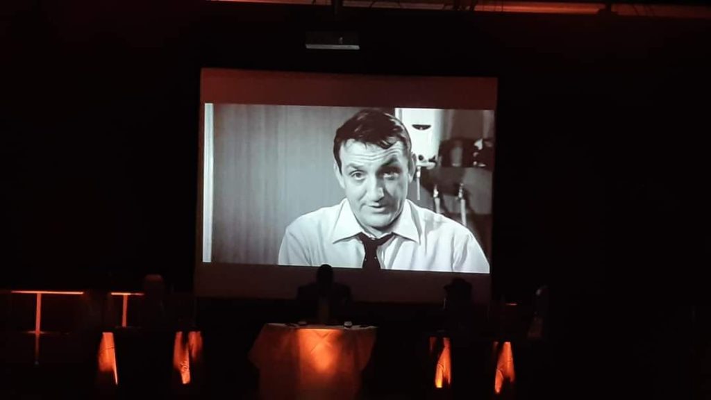 Inauguration du Théâtre Michel Audiard, projection en noir et blanc sur scène avec des intervenants au premier plan.