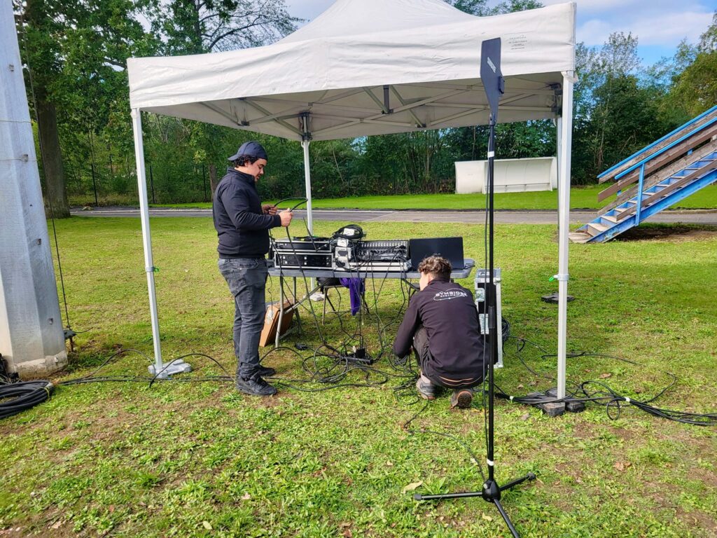 Deux techniciens installent du matériel audio sous un chapiteau lors de l'événement Sport en fête à la Celle Saint-Cloud.