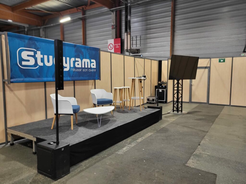 Scène de conférence avec chaises, table, écran et matériel de sonorisation au salon Studyrama à Paris.
