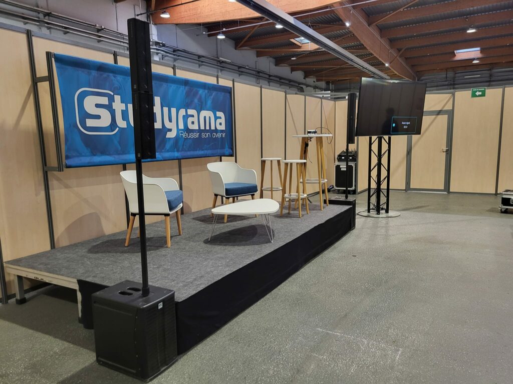 Scène de conférence avec chaises et écran à l'événement Studyrama, signalisation audio-visuelle présente.