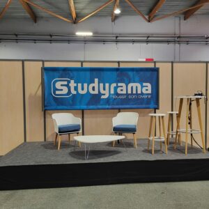 Scène avec logo Studyrama, deux chaises, tables et équipement de sonorisation dans un salon d'expo.