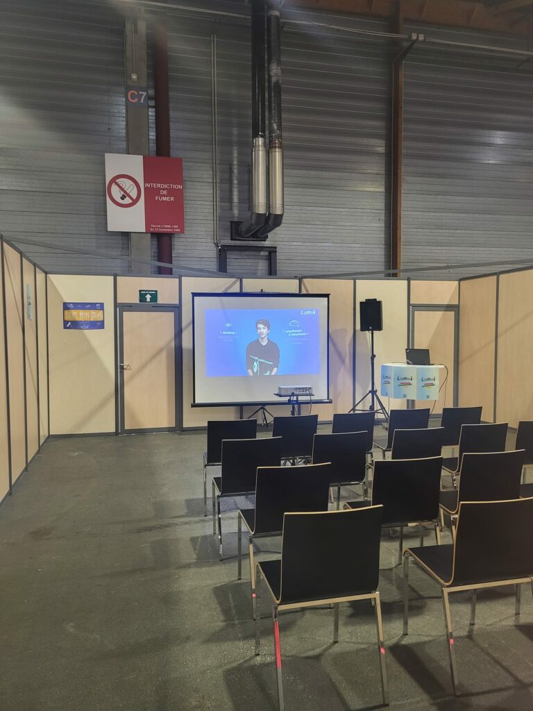 Salle de conférence à l'événement Studyrama à Paris avec chaises noires et écran de projection. Interdiction de fumer affichée.