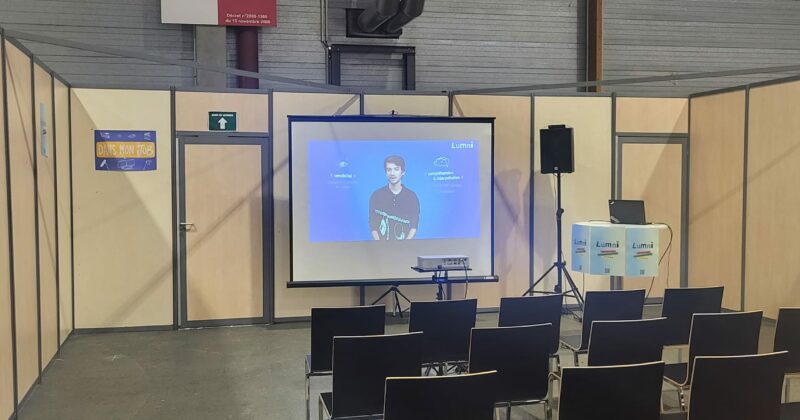 Salle de conférence à l'événement Studyrama à Paris avec chaises noires et écran de projection. Interdiction de fumer affichée.