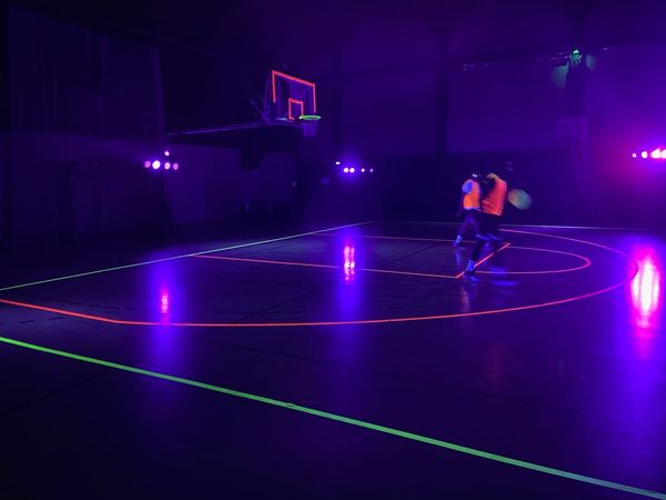 Match de basketball sous lumières UV, le 2 février 2024, avec un éclairage violet et des joueurs en action.