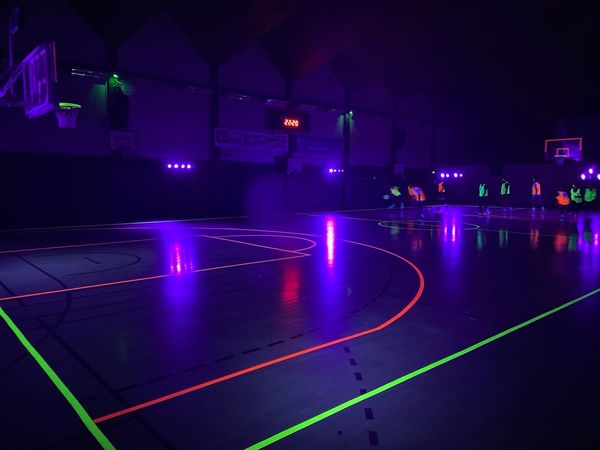 Terrain de basketball illuminé par des lumières UV, prêt pour un match sur le thème Ultraviolet le 2 février 2024.