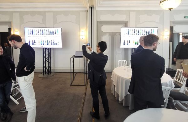 Participants à l'événement Pasona au Pavillon Ledoyen, regardant des présentations sur le saké. Écrans affichant différentes bouteilles.