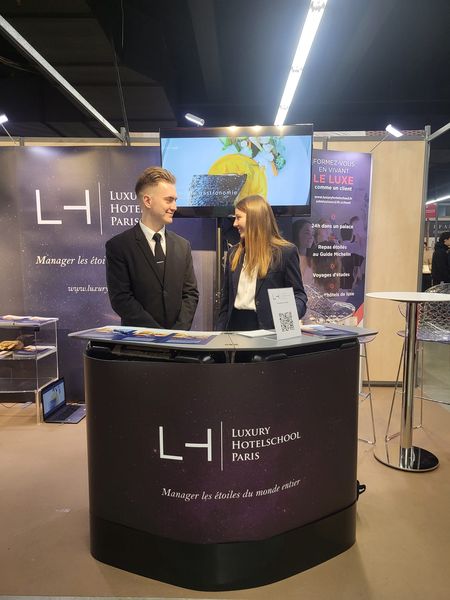 Deux personnes se tenant devant un stand de l'école de luxe Paris lors d'un salon d'exposition à l'espace Champerret.