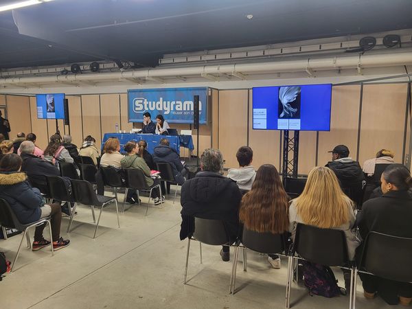 Conférence avec un public dans un salon d'exposition à l'espace Champerret, des écrans affichant des présentations.