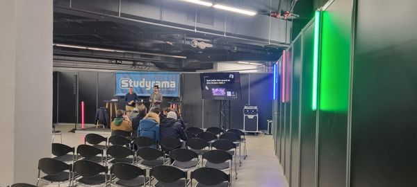 Salon Studyrama 2024 avec une salle de conférence, des spectateurs et un écran de présentation. Éclairage coloré en arrière-plan.