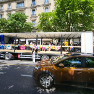 Char décoré de ballons pour la marche de Jésus, bien sonorisé, transporté par un camion jaune. Activité festive sur la route.