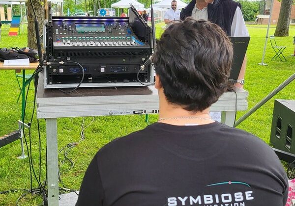 Technicien de son gérant un matériel audio pour les Olympiades de Neauphle-le-Château, avec une vue sur un parc et des tentes.