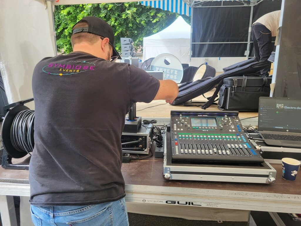 Technicien préparant la sono pour le concert à Houdan, avec mélangeur audio et câbles sur la scène.