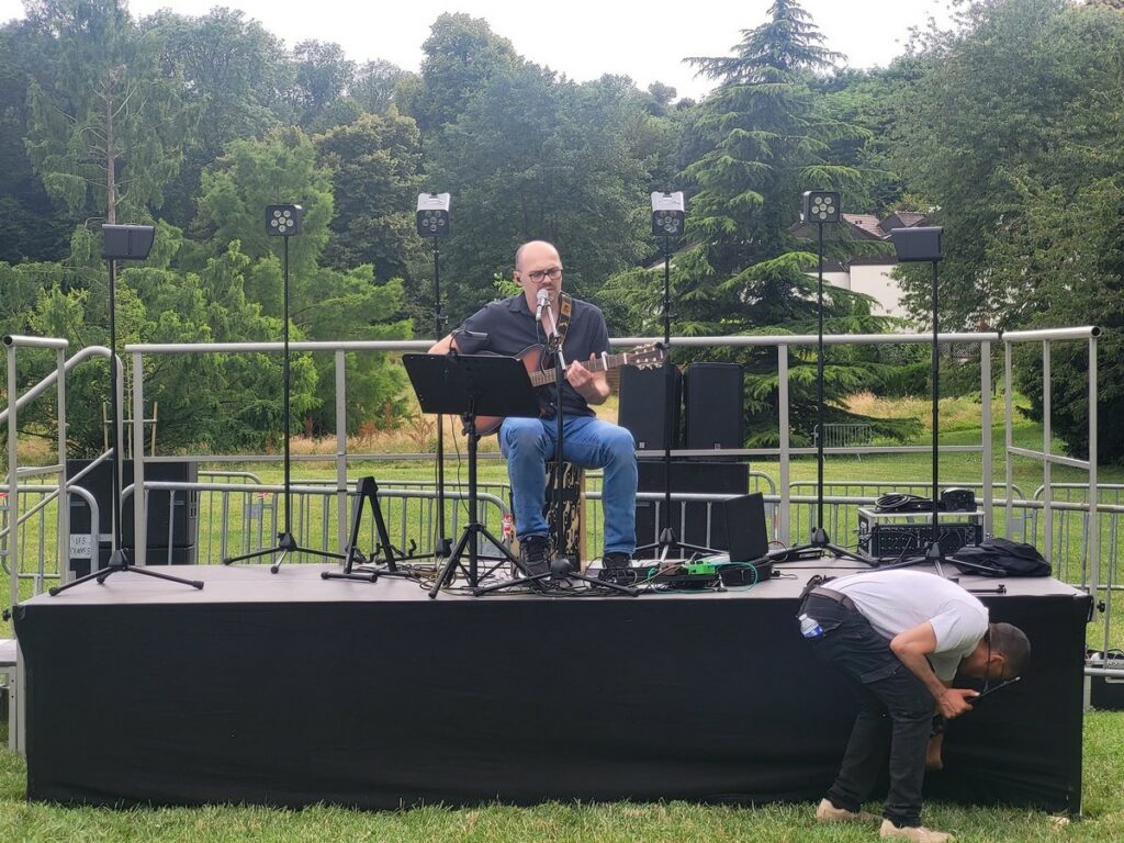 Musicien sur scène avec guitare, préparatif d'un événement en plein air aux Clayes-sous-Bois, sonorisation en cours.
