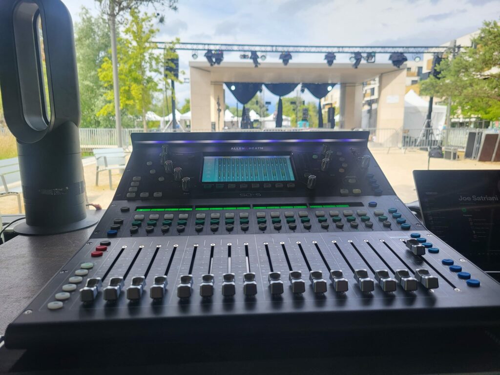Console de mixage en vue d'un événement extérieur, avec scène et éclairage en arrière-plan à Saint-Cyr-l'École.