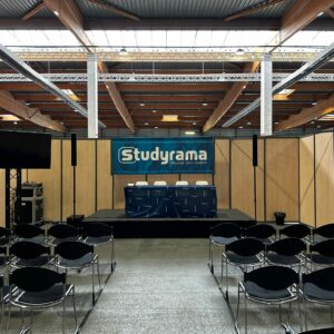Stand Studyrama avec des chaises noires, un podium et un écran, prêt pour un événement au sein d'un espace ouvert.