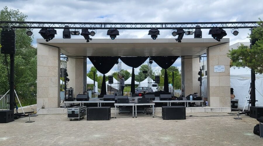Scène montée avec éclairage et matériel audio, prête pour un événement en extérieur.