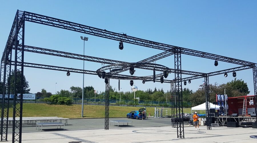 Installation de scène en métal noir avec éclairage, prête pour un événement en plein air.