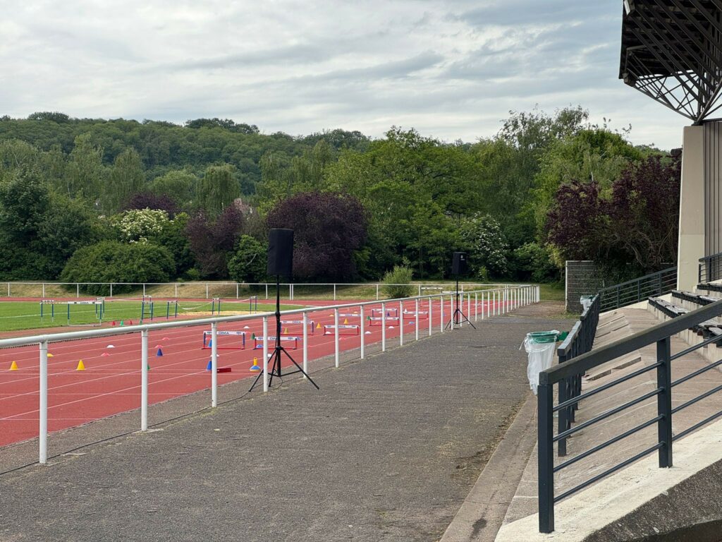 Installation de matériel de sonorisation sur une piste d'athlétisme, entourée de verdure.