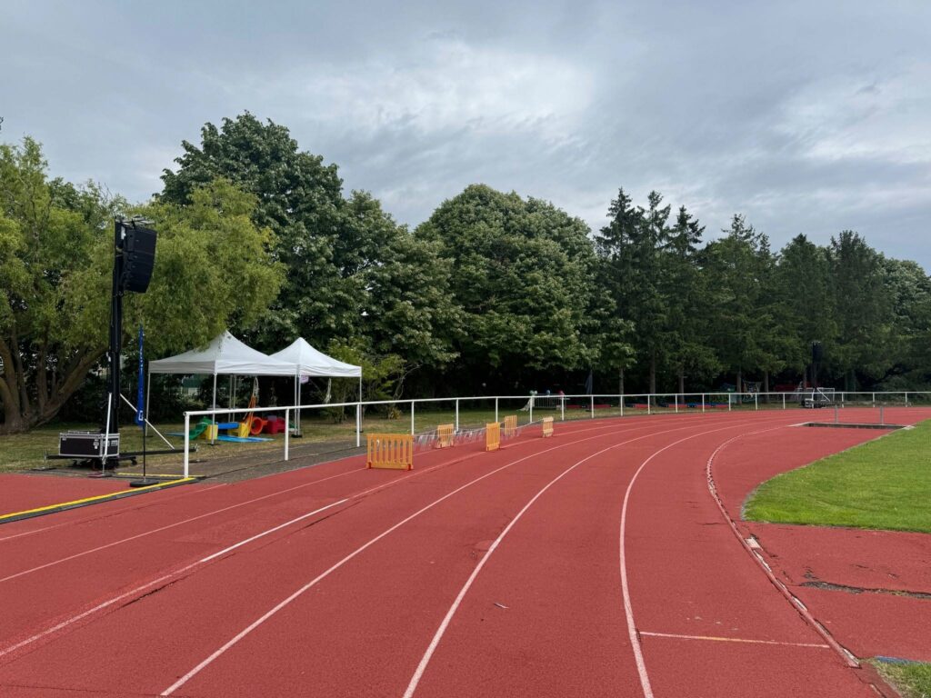 Installation de matériel de sono sur un terrain de sport, avec un chapiteau et des équipements couleur vive en arrière-plan.