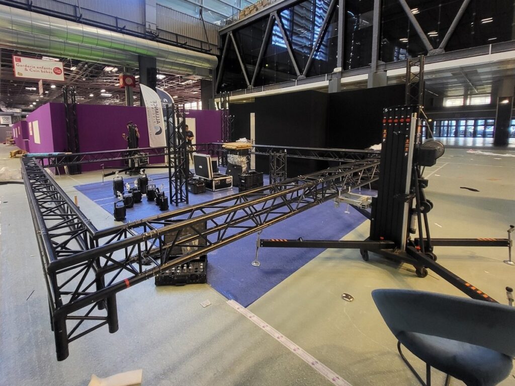 Installation de matériel de sonorisation et éclairage dans un espace événementiel avec structures métalliques et équipements.