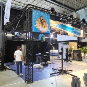 Stand d'exposition avec matériel de son et éclairage, affiches et préparation pour un événement, dans un hall.