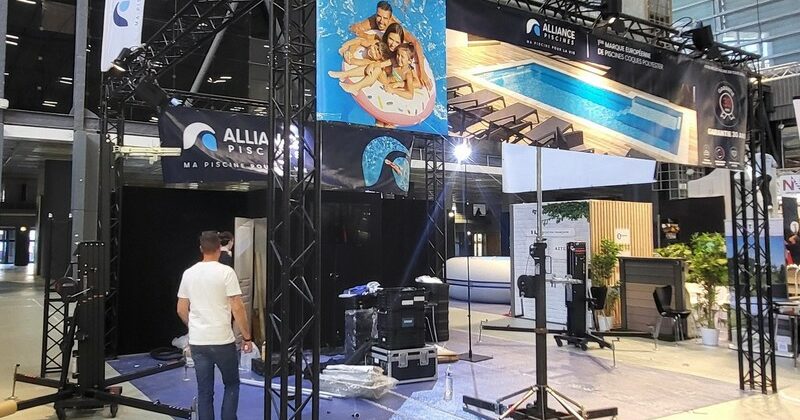 Stand d'exposition avec matériel de son et éclairage, affiches et préparation pour un événement, dans un hall.