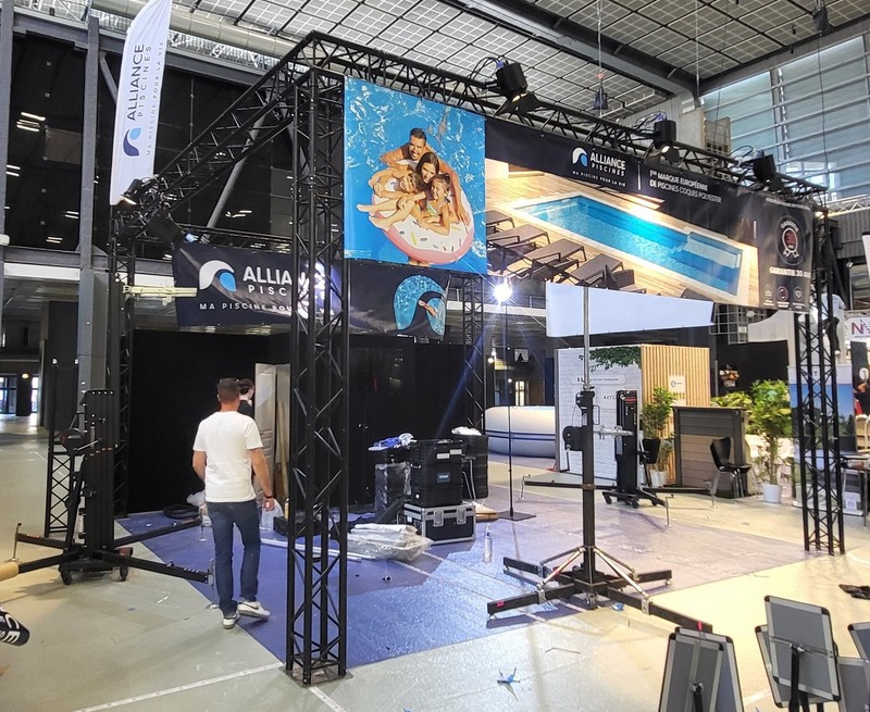 Stand d'exposition avec matériel de son et éclairage, affiches et préparation pour un événement, dans un hall.