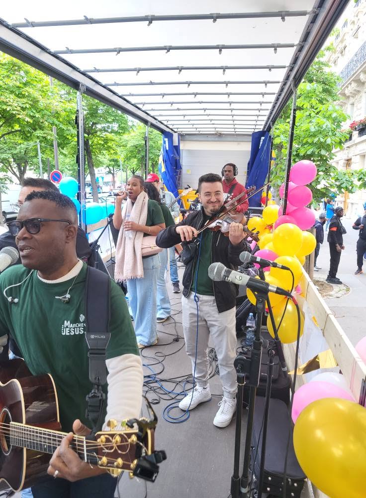 Musiciens sur un camion avec microphones et instruments, animant un événement festif en plein air, entourés de ballons colorés.