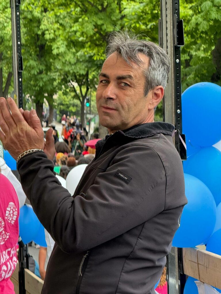 Homme applaudissant, en arrière-plan des ballons bleus, lors d'un événement en extérieur.