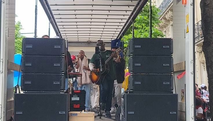 Concert en plein air dans un camion avec des musiciens et du matériel de sono visible.