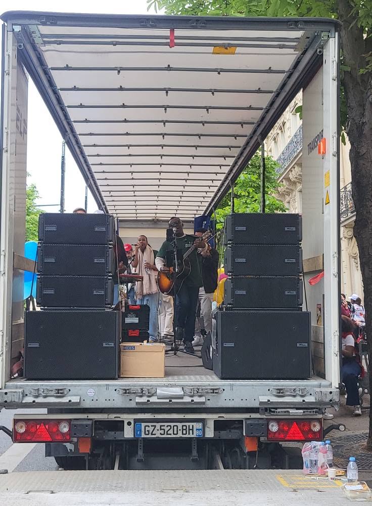 Concert en plein air dans un camion avec des musiciens et du matériel de sono visible.